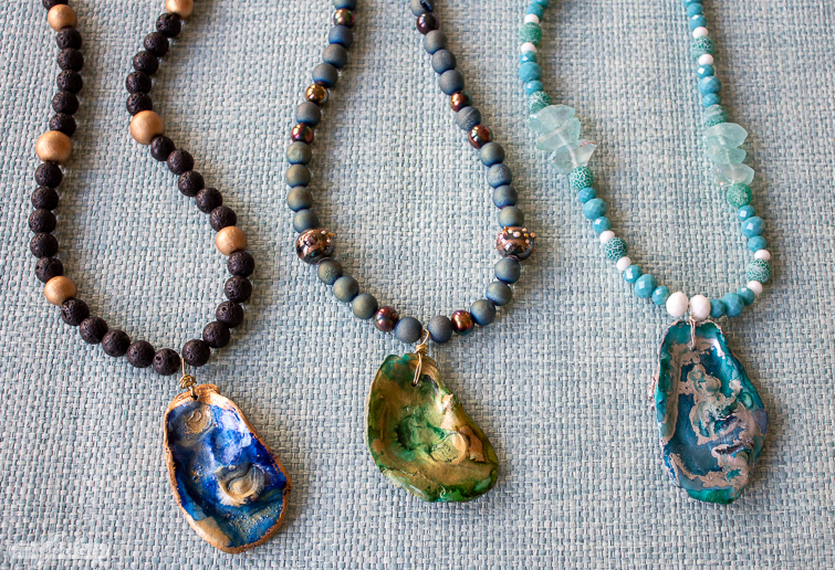 three alcohol ink oyster shell pendant necklaces on grasscloth