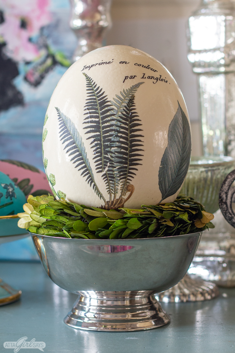 ostrich egg decorated with vintage fern leaf illustrations sitting in a silver bowl 