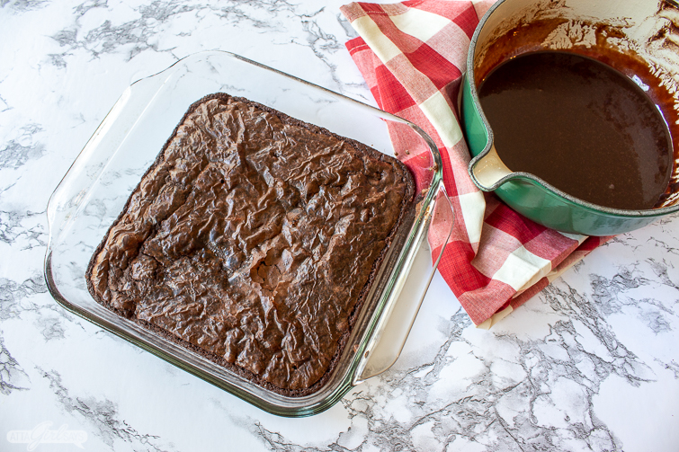 Ghiardelli triple fudge brownies in a glass pan beside a pan of chocoalte of brownie icing recipe