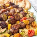 pork and vegetable kabobs over orzo pasta on an enamel tray
