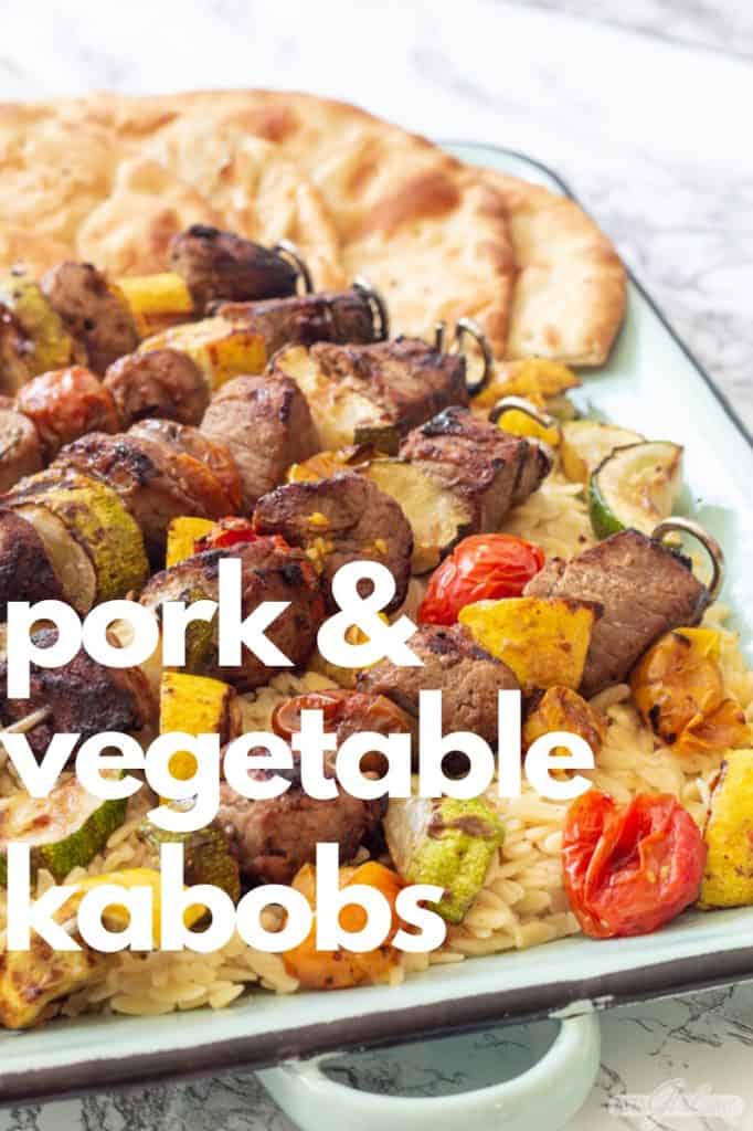 pork and vegetable kabobs over orzo pasta on an enamel tray