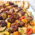 pork and vegetable kabobs over orzo pasta on an enamel tray