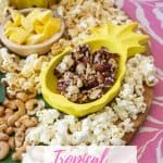 tropical charcuterie snackboard with mango, popcorn, nuts and nut clusters in a pineapple shaped bowl