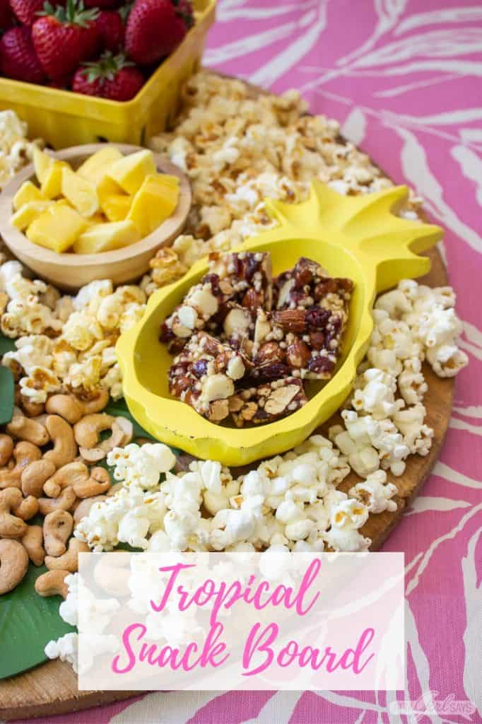 tropical charcuterie snackboard with mango, popcorn, nuts and nut clusters in a pineapple shaped bowl