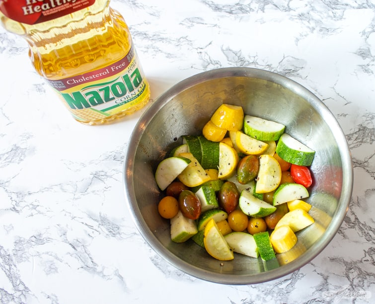 squash and colorful grape tomatoes marinating in oil and spices in a stainless steel bowl