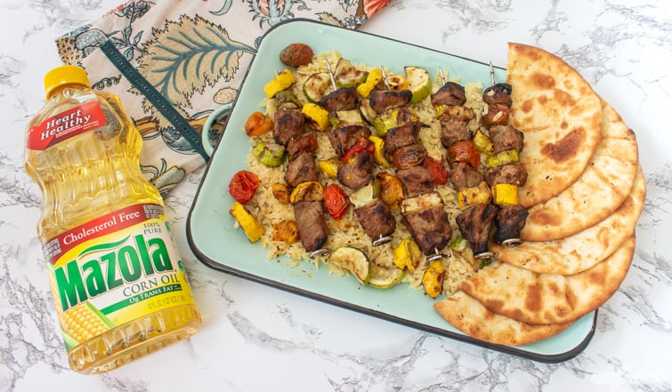 Vegetable and pork kabobs on a bed of orzo pasta with a bottle of corn oil