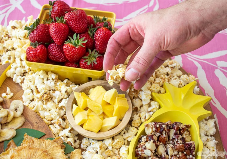 man's picking up popcorn off a tropical charcuterie board
