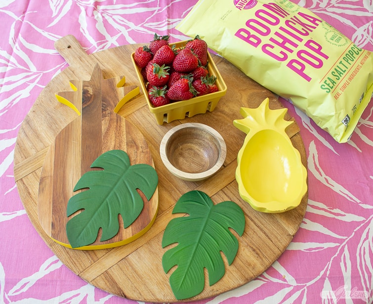 wooden snack board with strawberries, pineapple bowl and monstera leaves