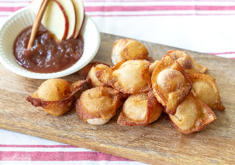 fried sweet cream cheese wontons on a wooden board with a bowl of apple butter