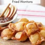 fried sweet cream cheese wontons on a wooden board with a bowl of apple butter