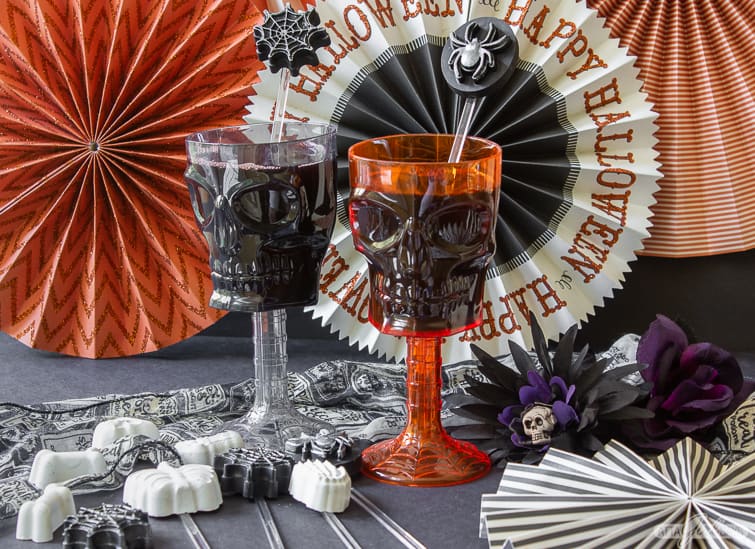two skull goblets with Halloween cocktail stirrers sitting in front of Halloween banners