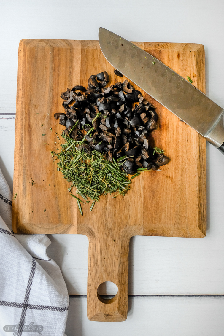 wooden cutting board with chopped herbs, capers and olives