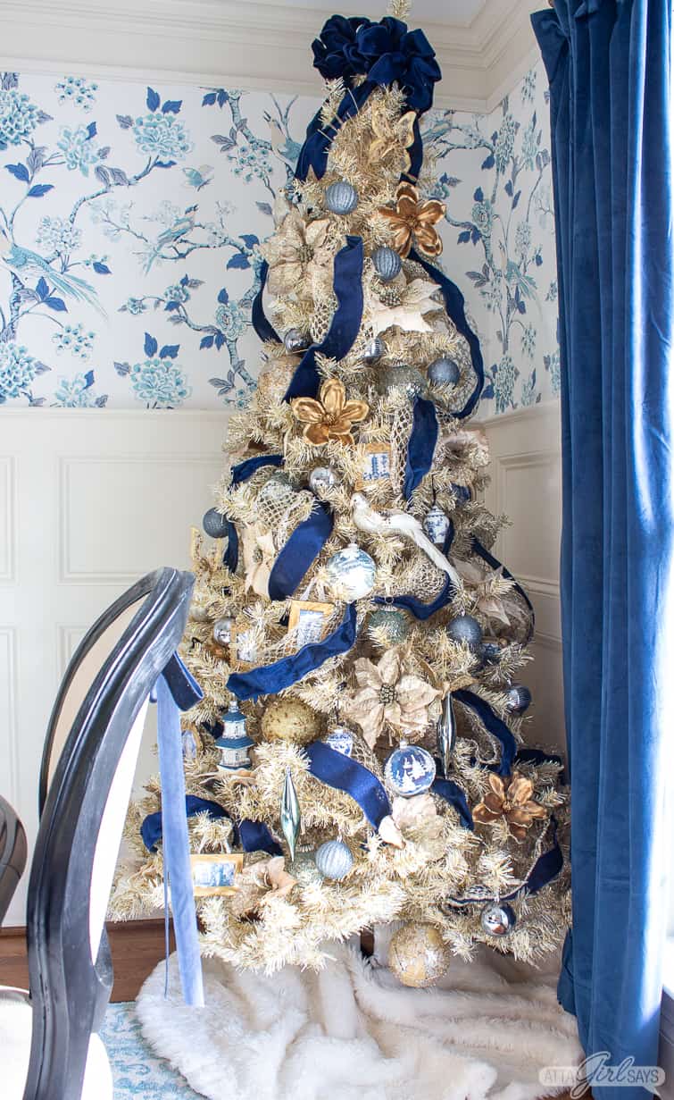 gold Christmas tree decorated with navy blue ribbon and blue and white ornaments against chinoiserie wallpaper