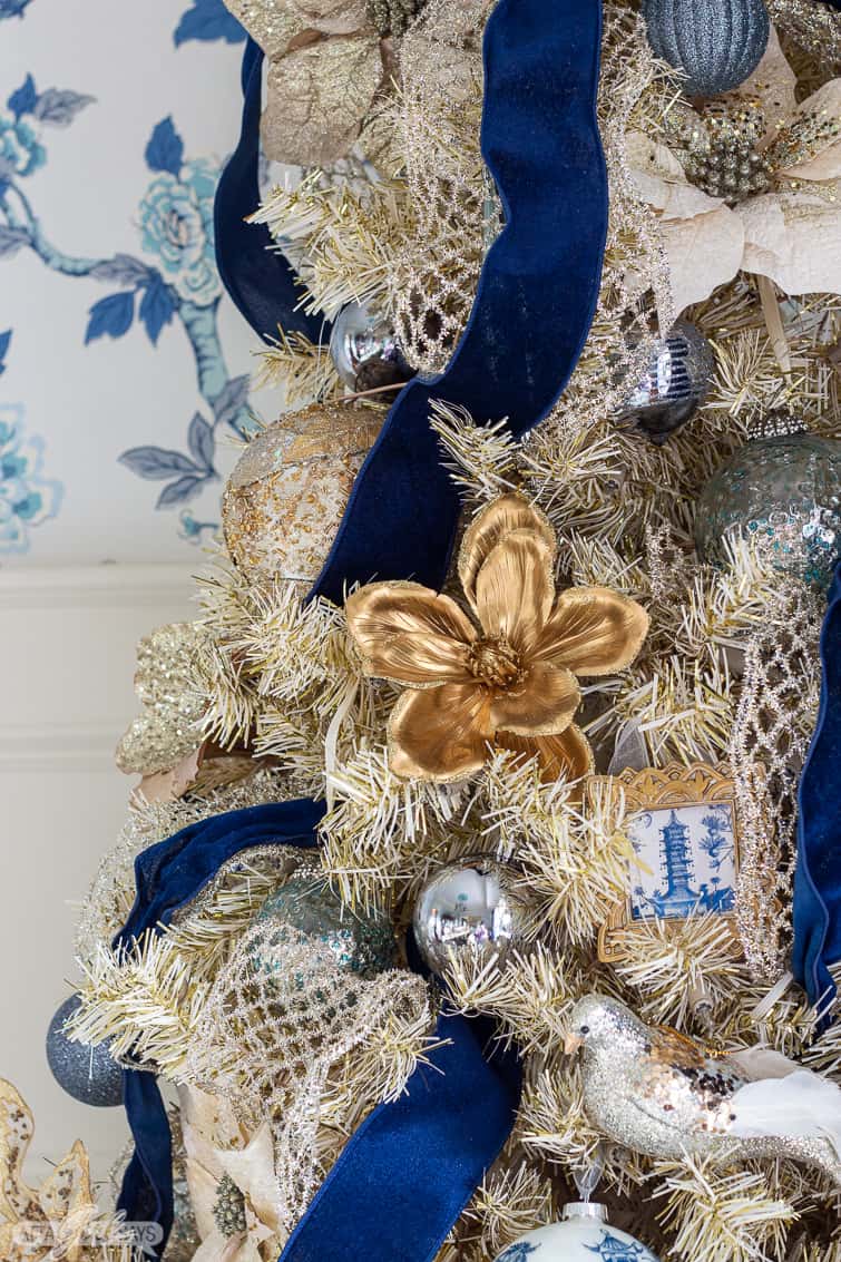gold Christmas tree decorated with navy blue ribbon and blue and white ornaments against chinoiserie wallpaper
