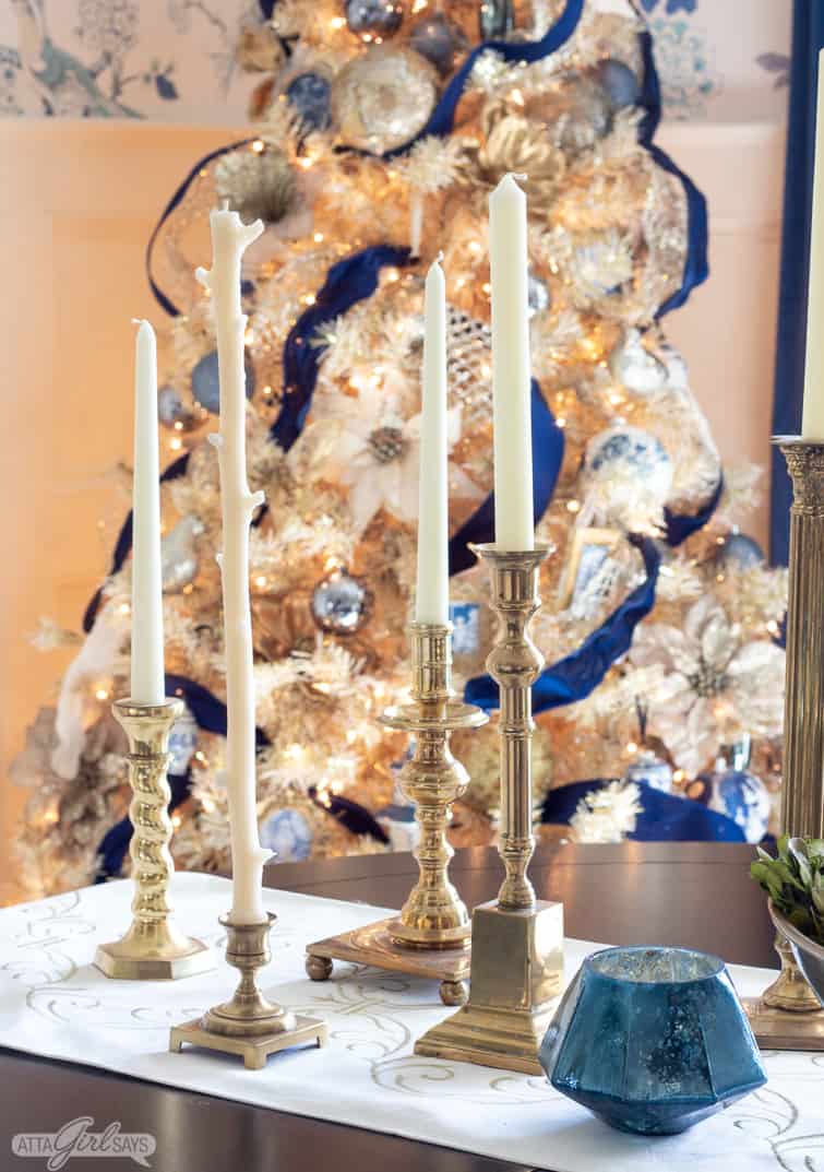 vintage brass candlesticks on a dining table with a glowing gold Christmas tree behind them