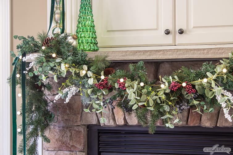 stone fireplace mantel decorated with a garland and green mercury glass trees
