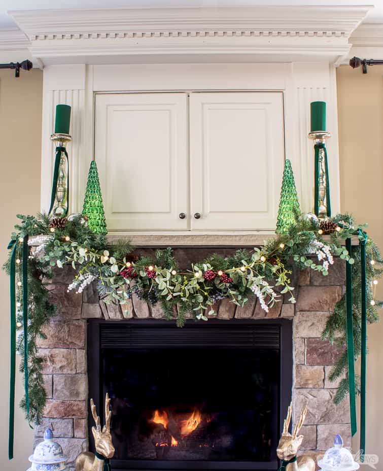 stone fireplace mantel decorated with a garland and green mercury glass trees