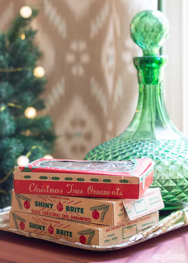 mini Shiny Brite ornament boxes stacked in front of a green glass decanter