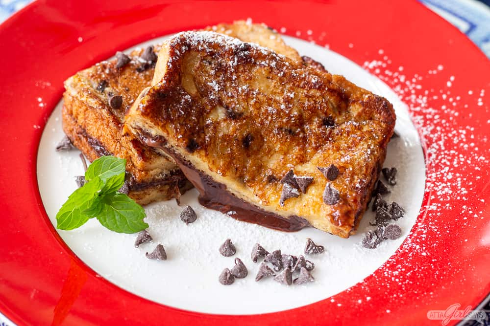 two half slices of grilled Nutella stuffed toast on a plate with chocolate chips and mint leaves
