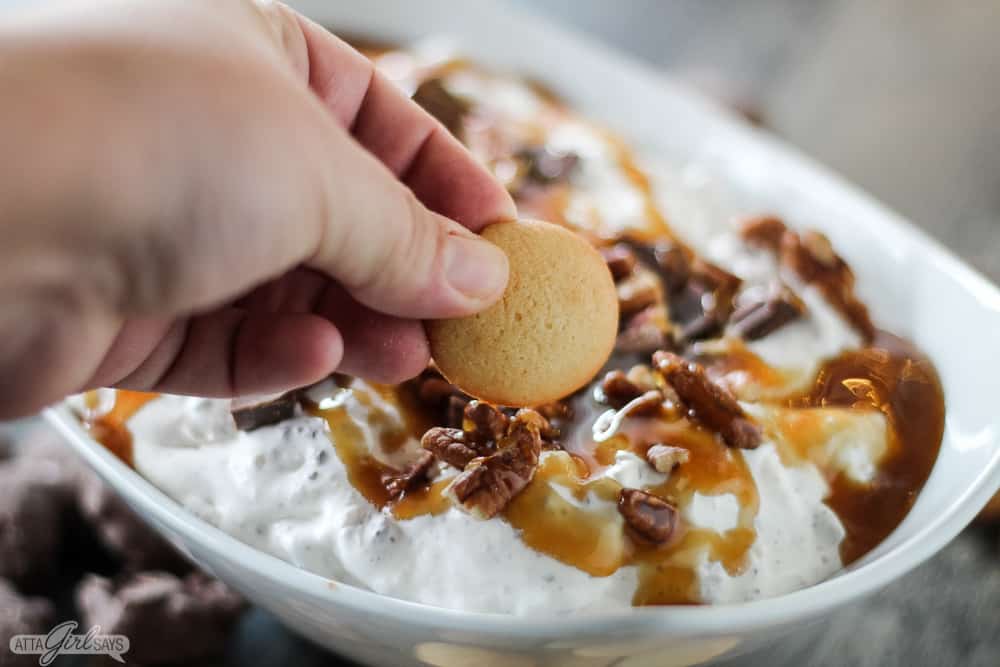 hand dipping a Nilla Wafer in turtle pecan chocolate cookie dip