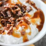 bowl of sweet cream cheese dip topped with pecans, chocolate and caramel