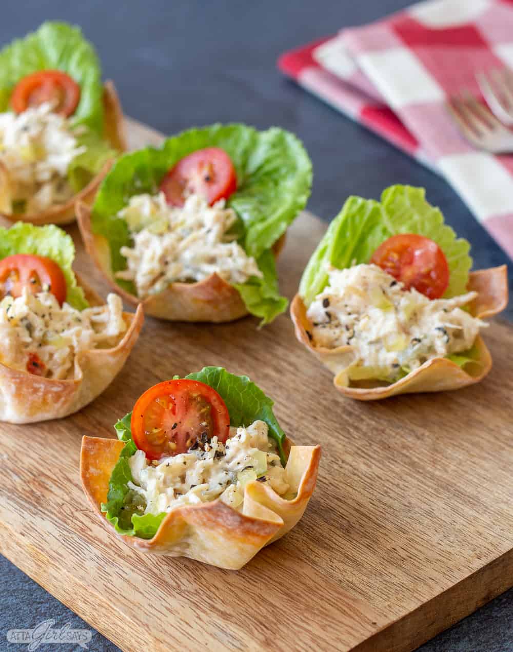 chicken salad wonton cups with lettuce and tomato on a wooden board