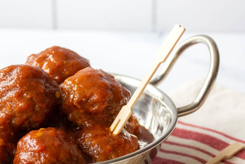 serving dish filled with meatballs on a red striped kitchen towel with serving picks