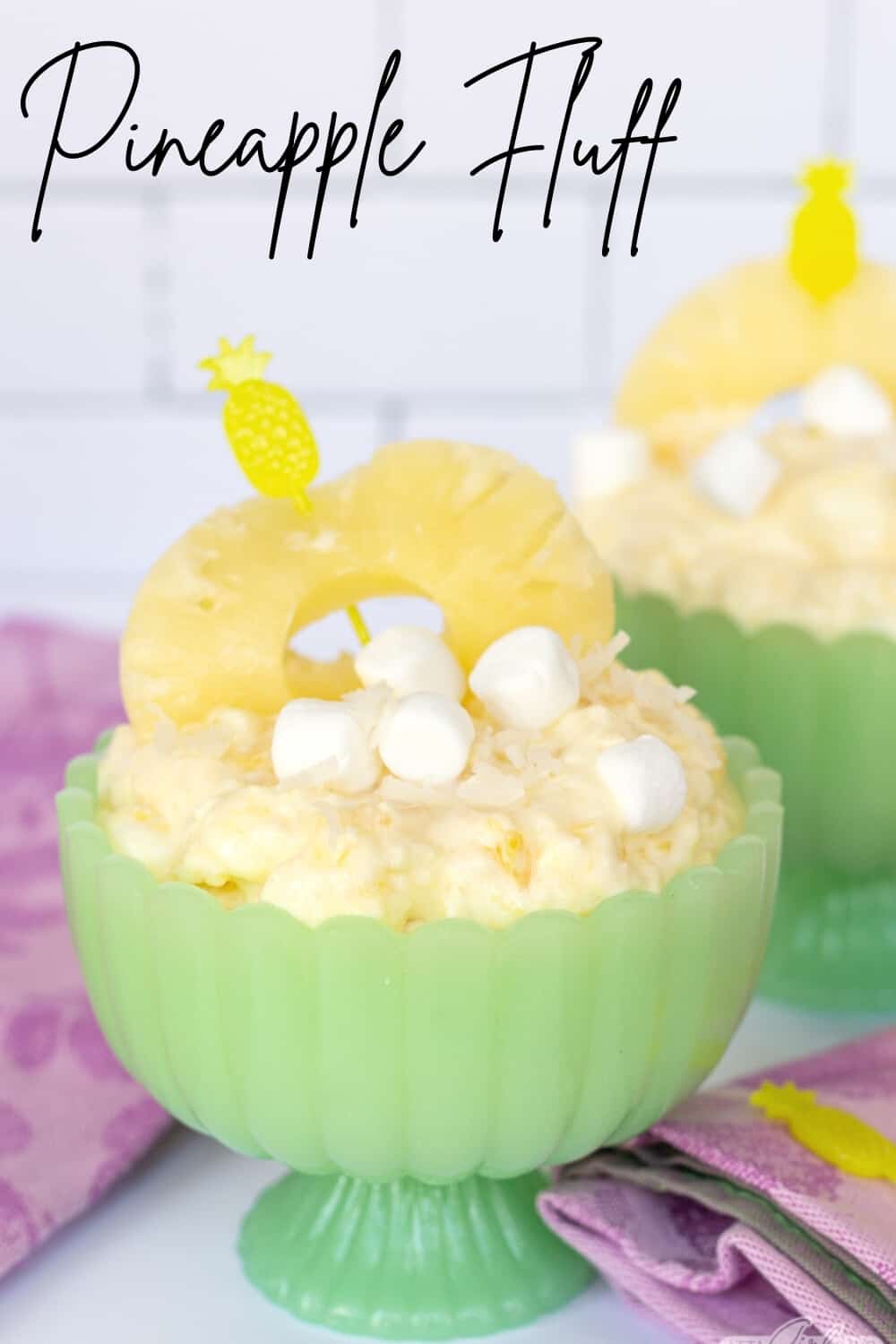 pineapple fluff garnished with marshmallows and pineapple ring in a green jadeite compote bowl
