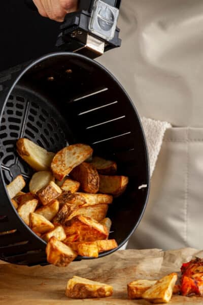 woman in apron pouring home fries out o an air fryer basket