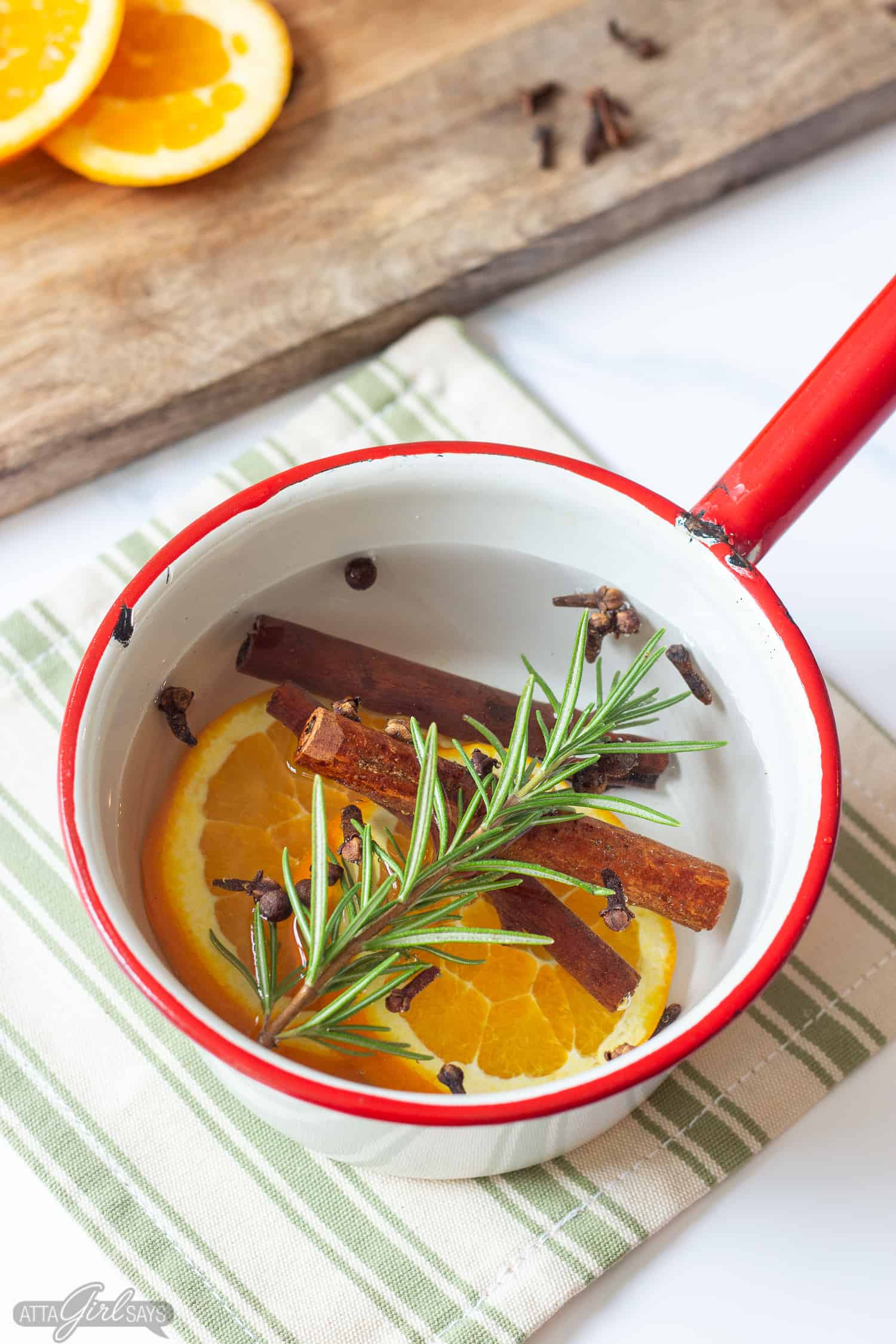orange slices, cinnamon sticks, spices and rosemary sprig in an enamel pan