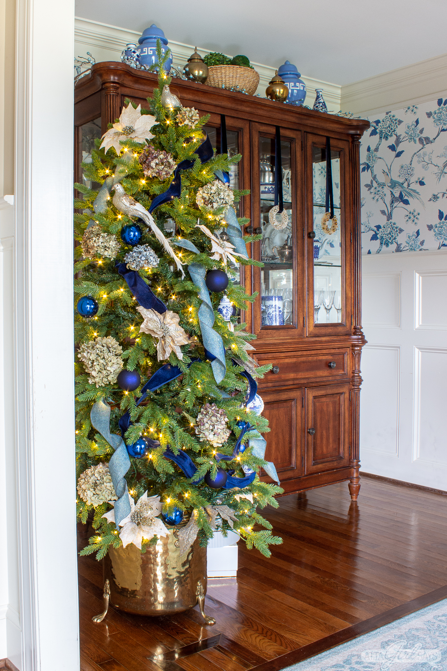 chinoiserie Christmas tree with dried hydrangeas beside a china cabinet in a dining room