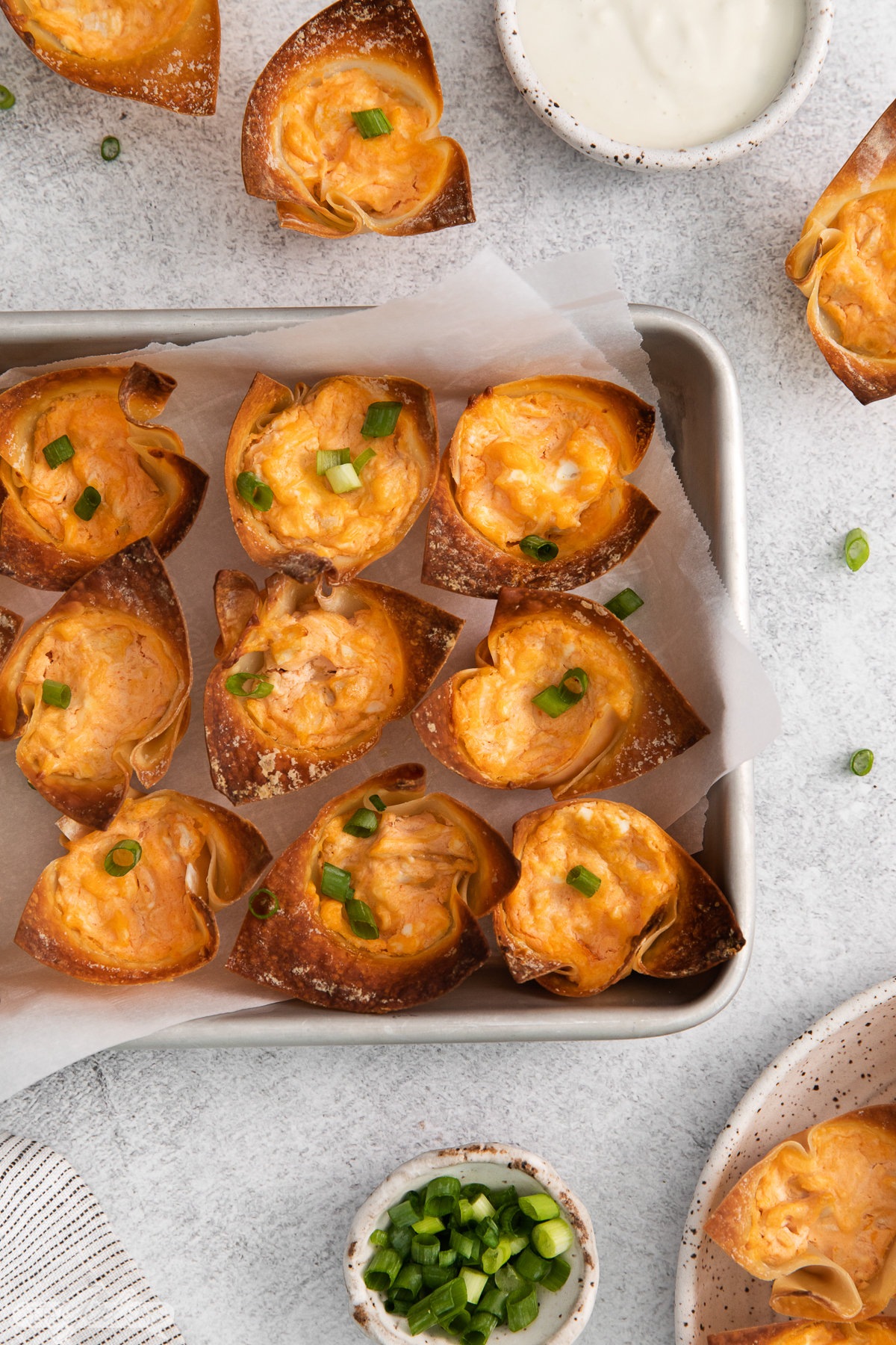 baked buffalo chicken wonton cup appetizers on a baking sheet with dip and green onions