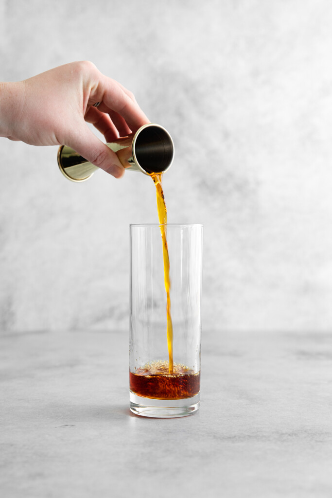 pouring dark rum into a highball glass
