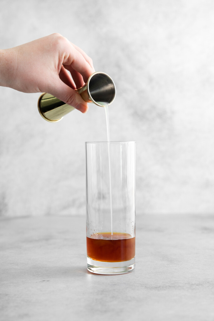 using a jigger to add lime juice to a highball glass with rum