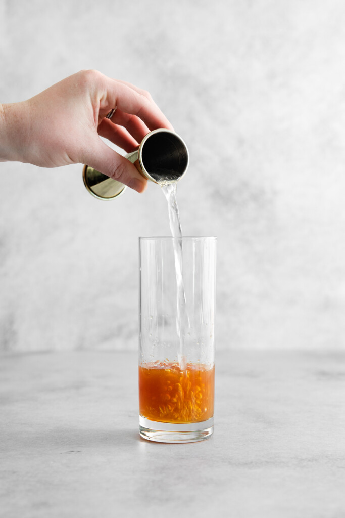 using a jigger to add ginger beer to a highball glass with rum