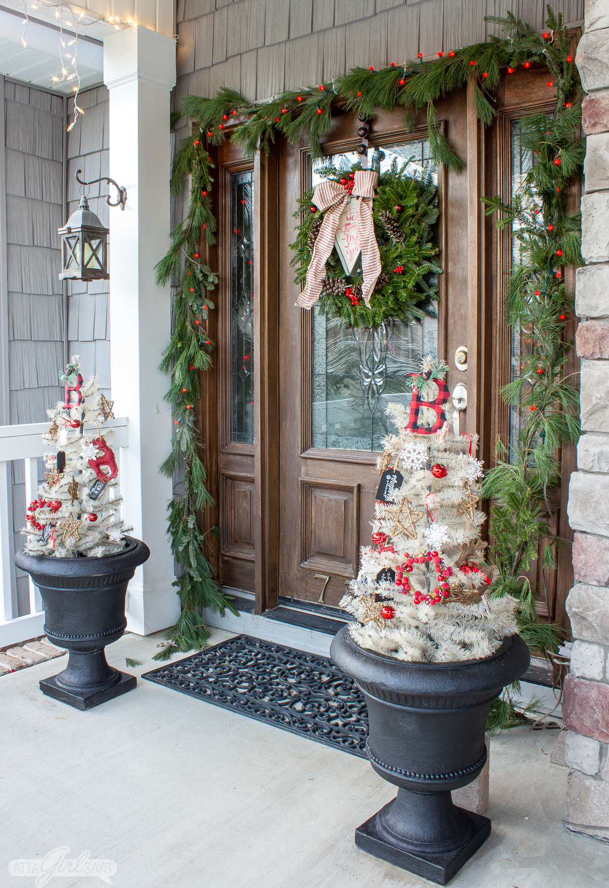 white trees in urns flanking a front door with a garland and wreath for Christmas