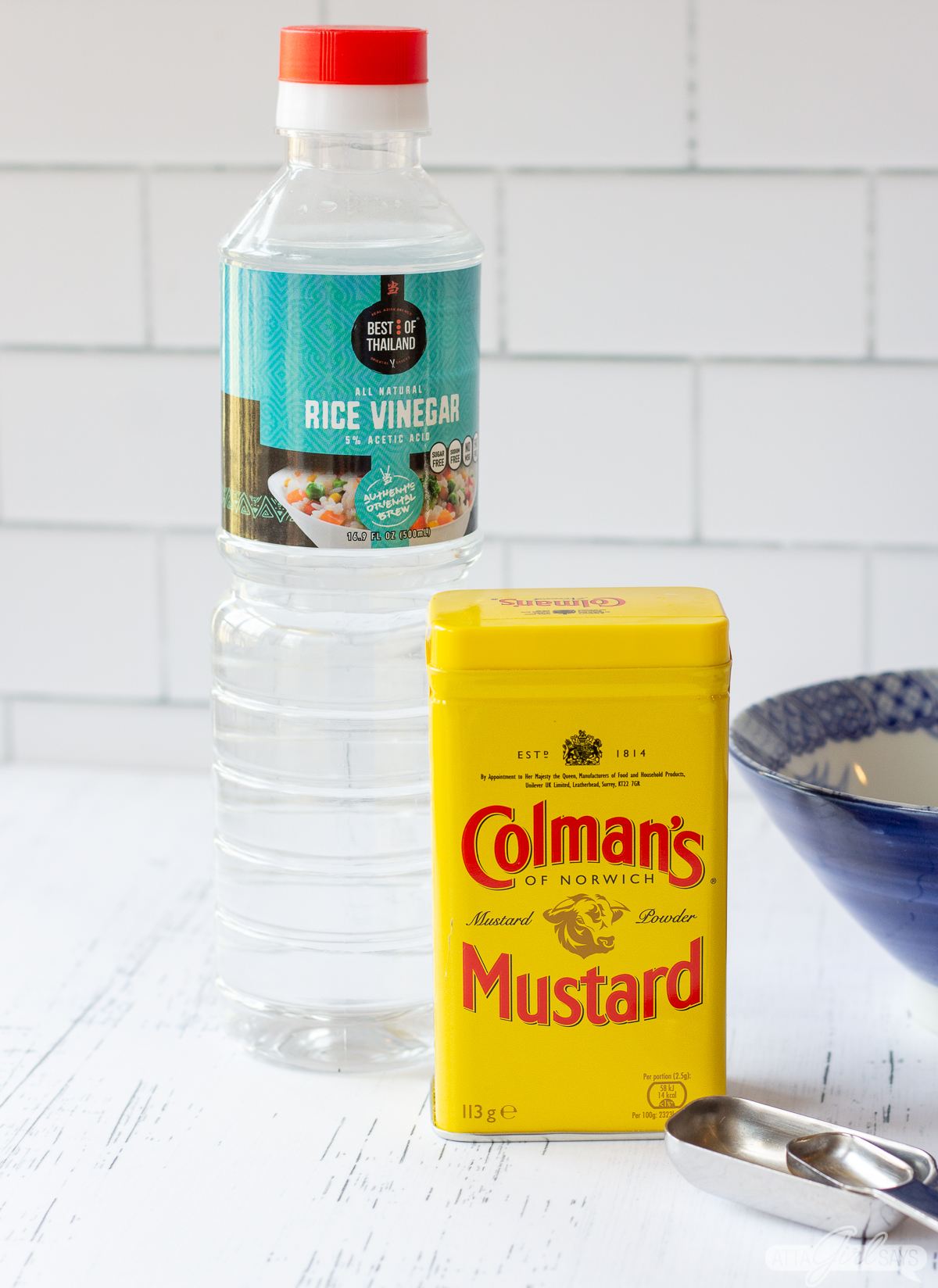 rice vinegar, Colman's mustard powder, a blue bowl and measuring spoons on a kitchen counter