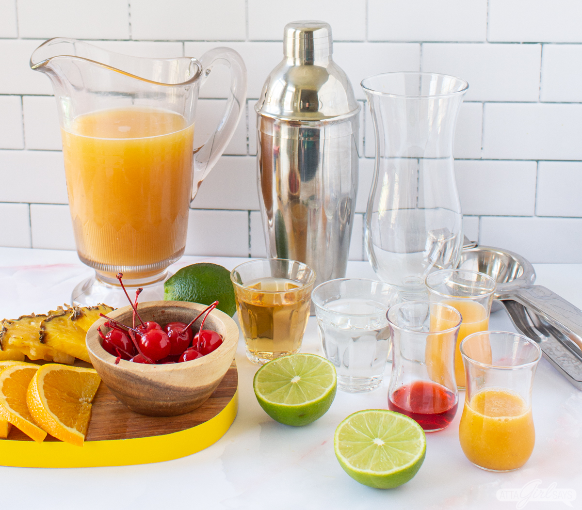 pitcher of POG juice with cherries, orange slices, pineapple slices, rum, cocktail shaker, sliced lime. passionfruit puree and grenadine in place to make a cocktail