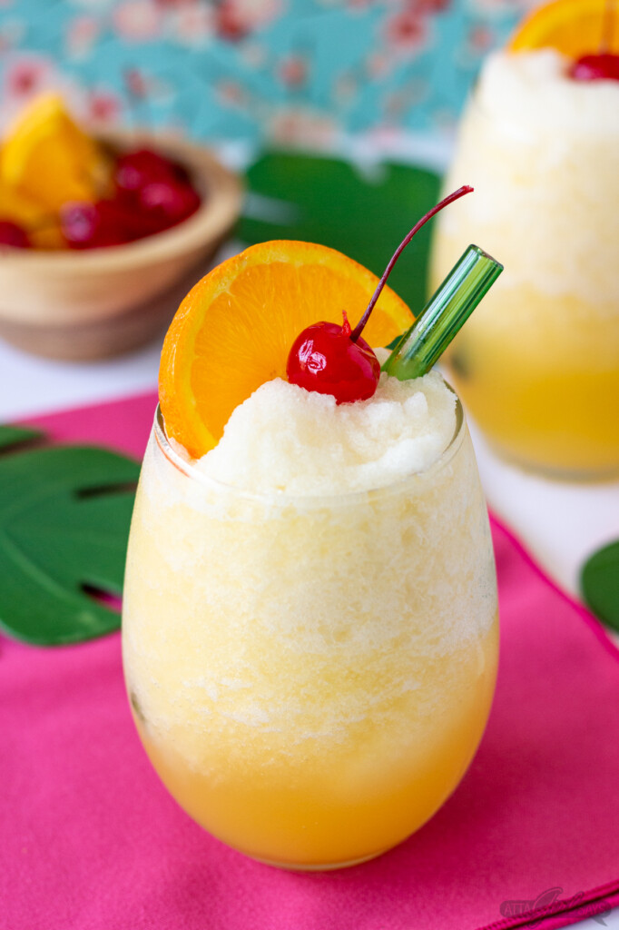 tropical wine slushie in a stemless glass with orange slice and cherry garnish
