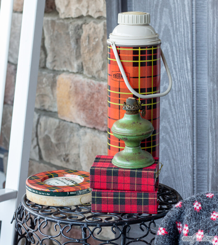 plaid Thermos, plaid tin tape dispenser, plaid books and a green lantern on an outdoor table