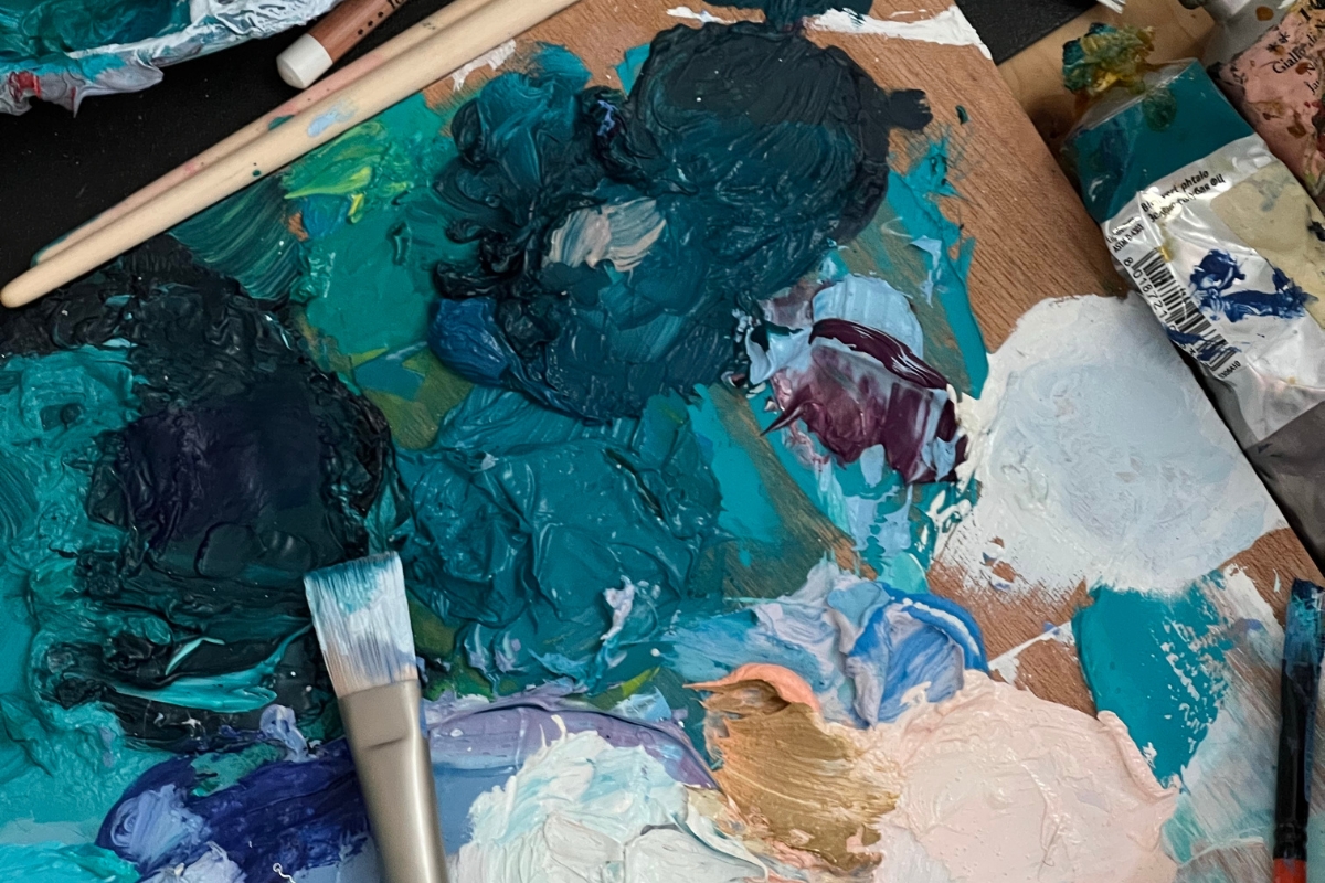 artist palette and brushes with piles of oil paint in shades of aqua blue and teal 
